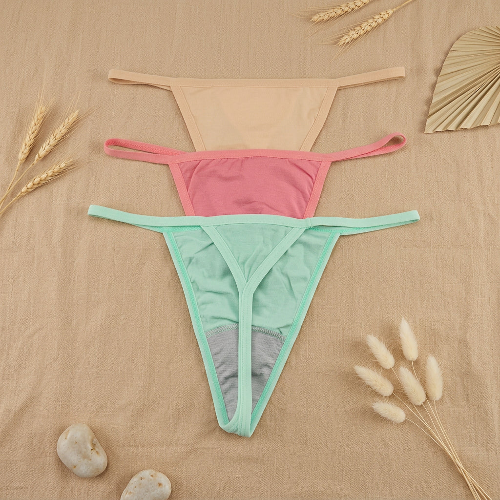 Three pairs of thong-style underwear laid flat on a gray surface, shown in beige, pink, and mint green.