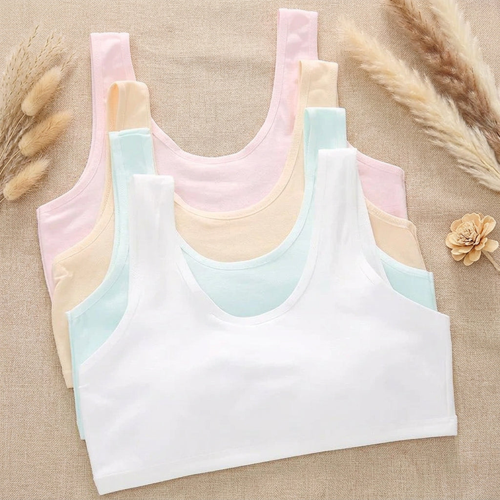 Four sleeveless ribbed tank tops in white, light blue, pale yellow, and light pink, arranged in a fan shape on a mint green background with printed papers and a small jar of blue beads.