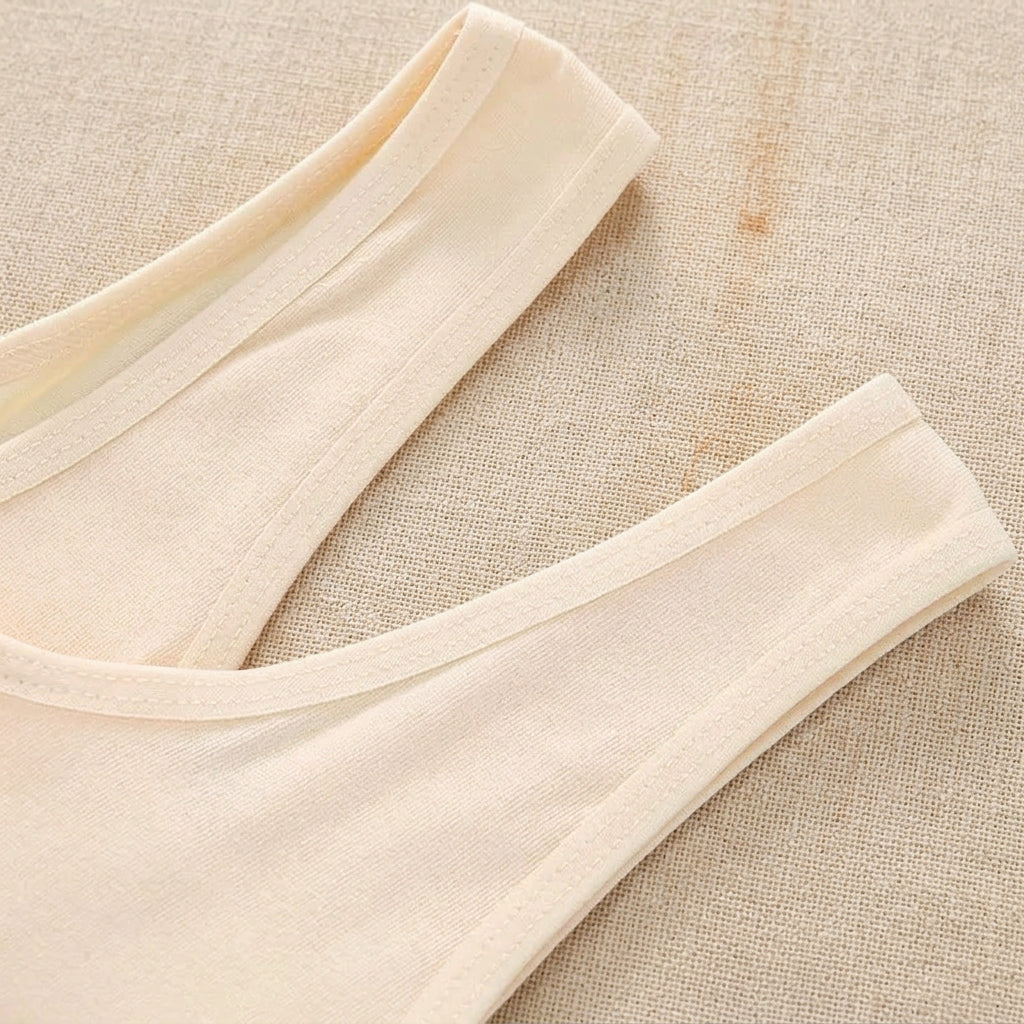 Close-up of a light beige or cream-colored tank top showing the scoop neckline and ribbed trim, laid flat on a mint green background.
