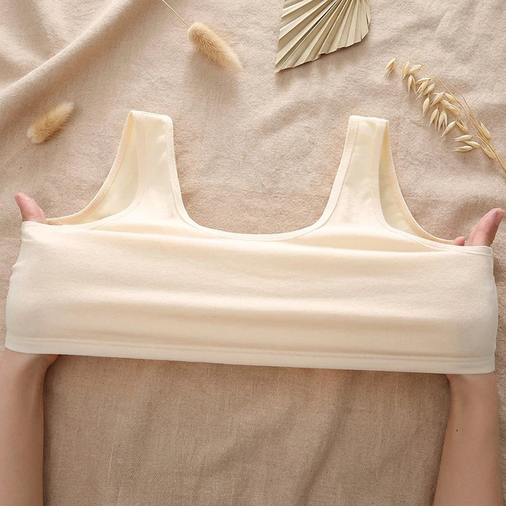 A light beige wireless bralette held open by two hands against a solid mint green background.