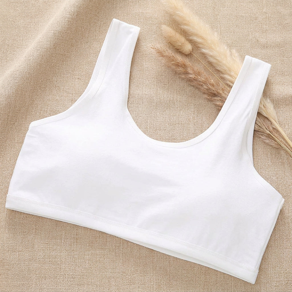 A white scoop-neck tank top laid flat on top of an open magazine page, set against a light mint green background.