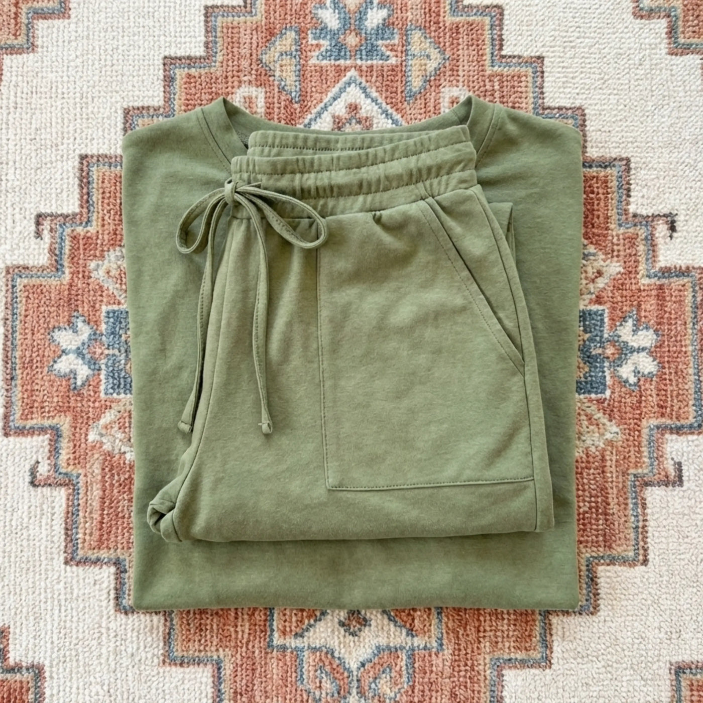 Folded green sweatpants on a patterned rug